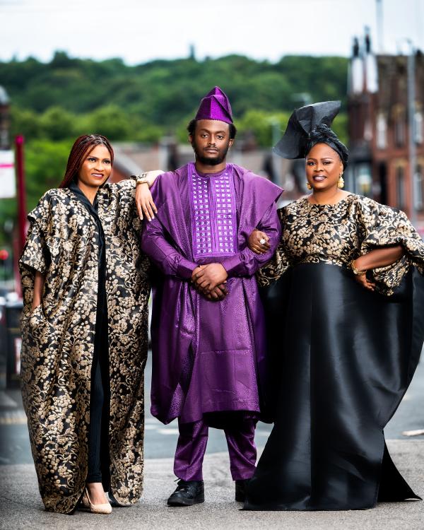 Two women and a man. The women are wearing Black and Gold Tunics and the man is wearing a Purple African traditional outfit.