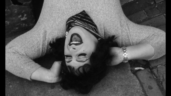 A black and white image of a person in drag lying with their hands behind of their head laughing