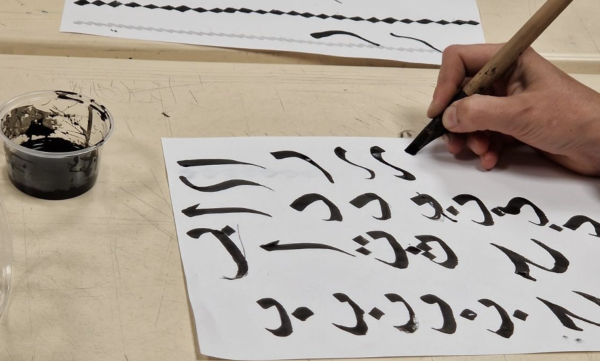 Arabic text being drawn in black ink