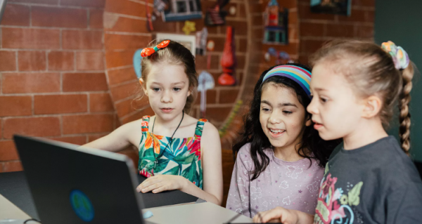 Three children look at a laptop screen.