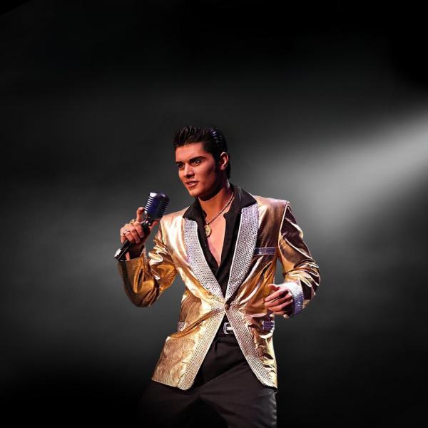 Elvis tribute act with the classic Elvis black quiff in a golden suit jacket, wide open black shirt underneath, black trousers and holding a retro-looking microphone.