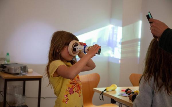 A child looks through a kaleidoscope while a project plays behind them.