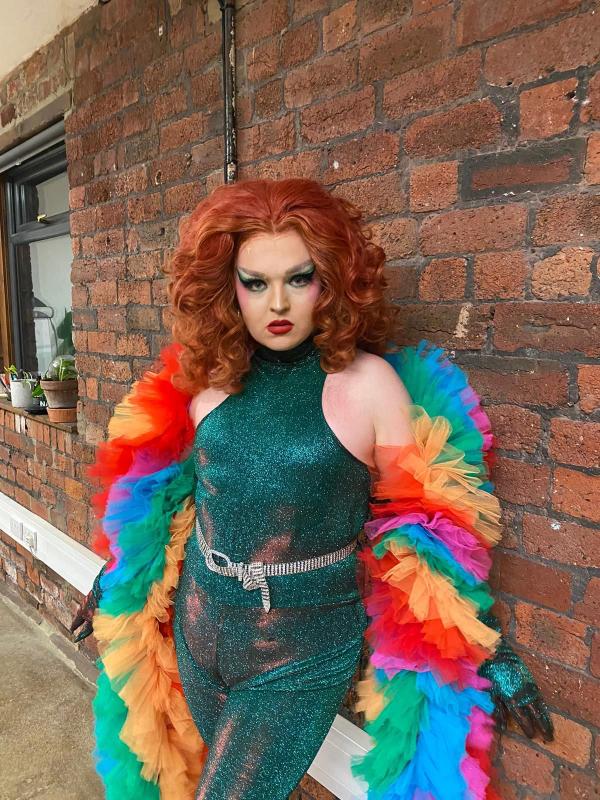 Pride Quiz Host and Drag Queen Sue Pertrouper wearing a fabulous outfirt and rainbow feather boa