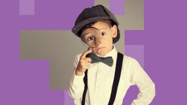 Young boy dressed in deerstalker hat with magnifying glass.