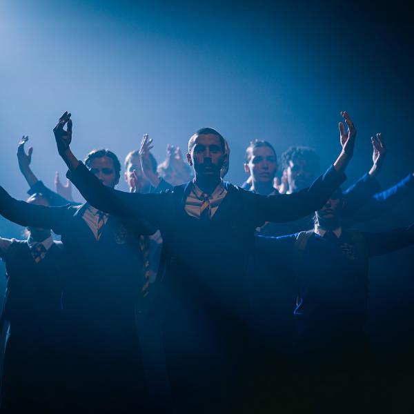 Group of dancers wearing school uniforms in triangle formation with their arms curved upwards