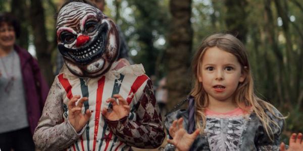 A child in a scary clown mask stands alongside a girl with fair hair in fancy dress, both grimacing