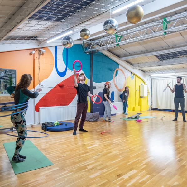 photo of the upstairs space at open source arts, here open circus training is in full swing. Participants are practicing hula hoops, juggling skittle, balls, frisbees and balancing on a wobble board