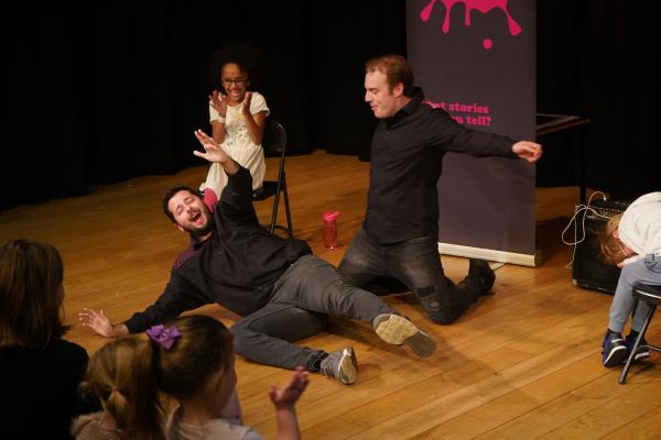 2 men frolic on stage as delighted children laugh and clap