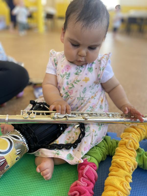 A toddler sitting on the floor holding a flute with a small drum on her lap