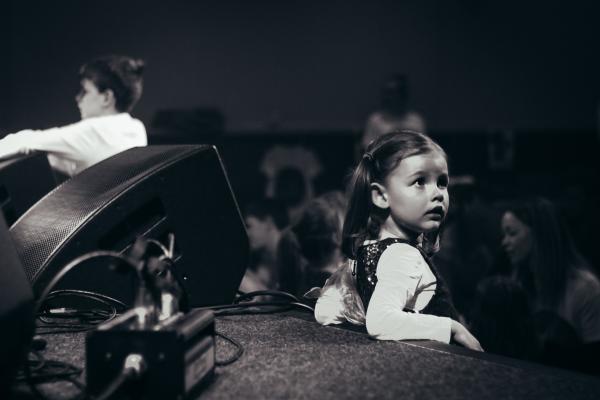 Young girl leaning against the stage next to a speaker, the photo is in black and white.