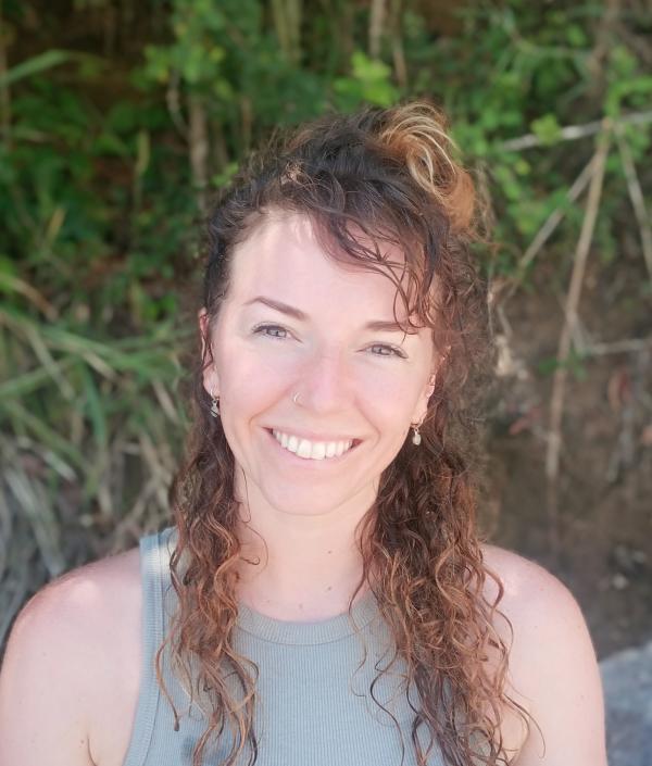 Keavy, portrait of her face, smiling looking at the camera, wide smile, plants in the background. An Earthy vibe