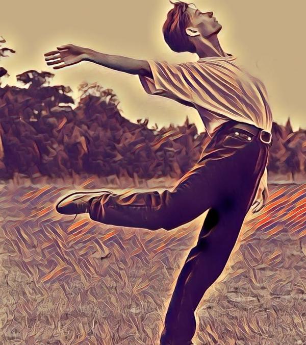 A young dancer in a field looking to the sky as he stretches his right arm back behind himself at shoulder height and his right leg bent behind him at knee height. 