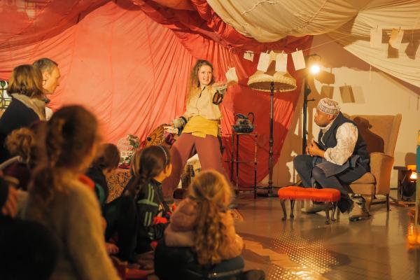 Photograph from The Storymaker’s Apprentice by Libellule at Leeds Central Library in 2022, Tan the main character is showing Mr Barwick something as part of the story with the audience watching on in wonder. Tan will also feature in the new show The Stolen Stories of Winterlight. 