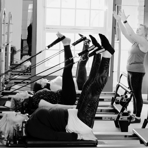 PIlates studio in black and white, the image shows a teacher teaching some women on a Pilates reformer 