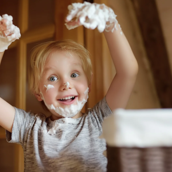 A photo of a child with shaving foam covering their hands and making a beard on their face