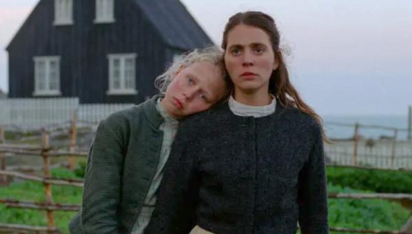 Still from Godland two characters leaning against each other in front of a house