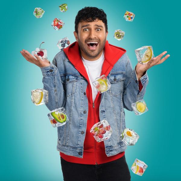 Shabaz Ali wearing a denim jacket over a red hoodie looking excited as ice cubes with fruit inside fall from the sky.