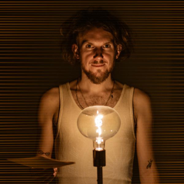 Atmospheric photo of a man in a vest by a lightbulb holding papers. 