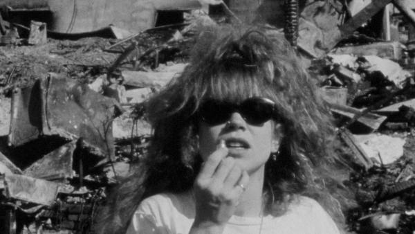 An image of a women, the titular character in I Was A Teenage Serial Killer, in black a white, looking at the camera and putting on lipstick. 