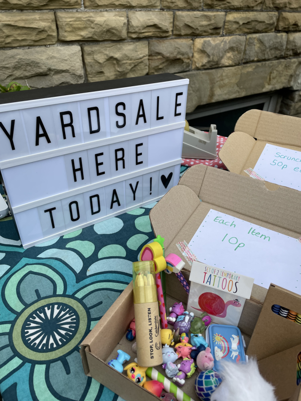 Photo features a stall from last years event with a sign saying Yard Sale Here Today along with a box of 10p items for sale