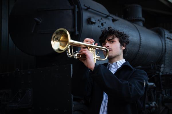 Peter from Indignation Meeting playing his trumpet in front of a steam train