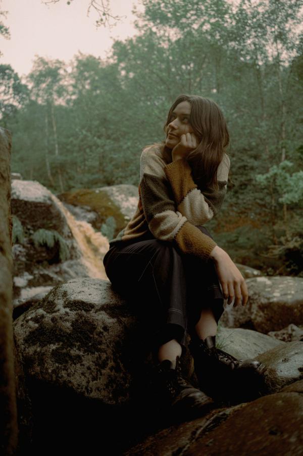 Marnie Glum sits on a rock resting her chin on her hand beside a mountain stream in some woods