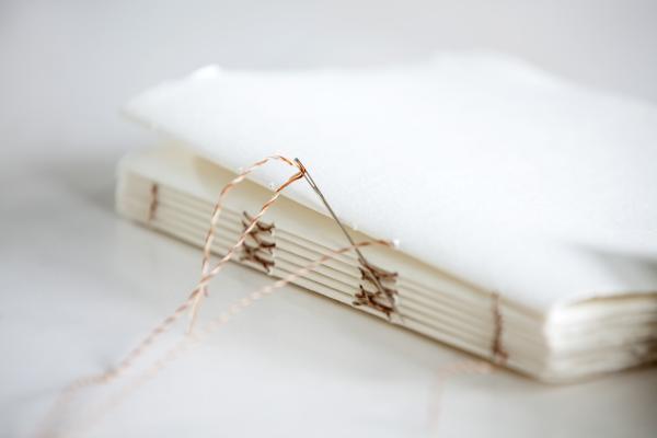 layers of white card being sewn together with a needle and thread 