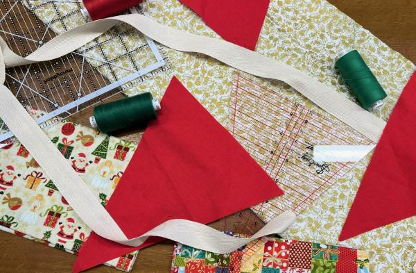 Red triangle fabric on top of Christmas fabrics surrounded by green and red thread