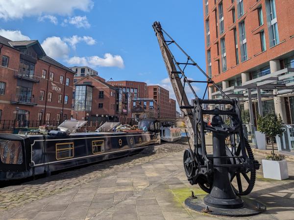 A docked narrowboat next to a heritage crane and surrounded by buildings and blue sky at Granary Wharf in Leeds