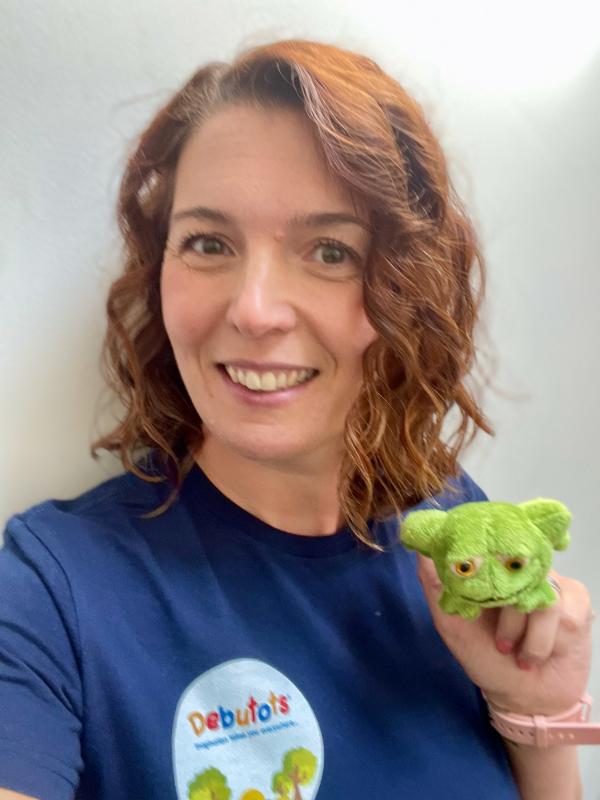 Female with brown hair holding a frog puppet.