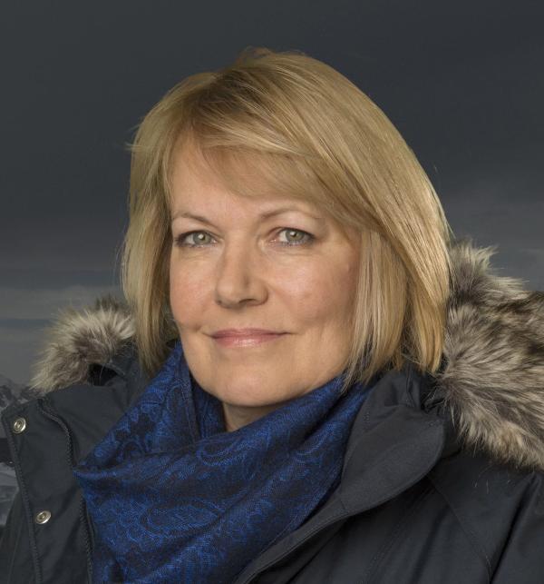 A headshot of a woman in her 50s smiling at the camera with short blonde hair and a winter jacket on with a fur trim.