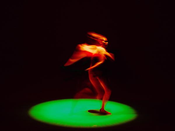 An illuminated orange figure runs on a green spotlit circle