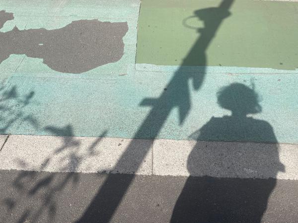 A photo of green paint on tarmac, and a shadow of a person next to a lamppost