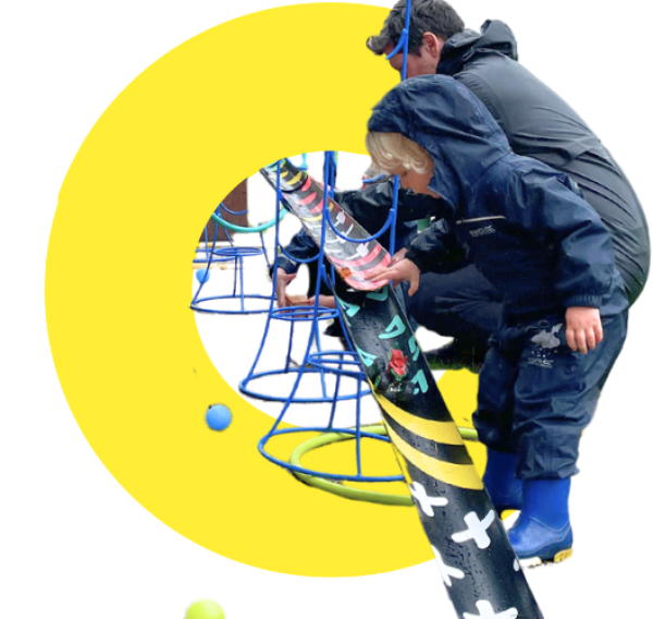 A photograph of a child and parent building a ball run on a yellow background