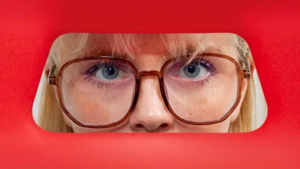 The close up of a person's face with blond hair, blue eyes and glasses.