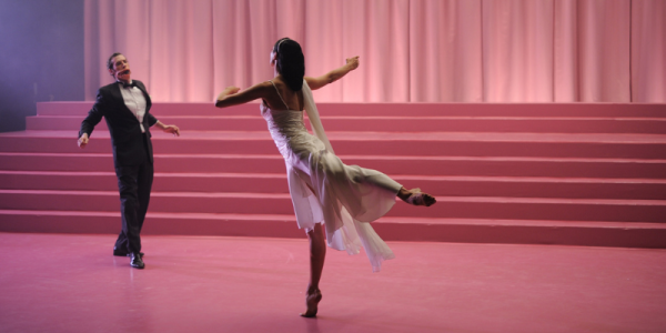 A man and woman dance in a pink theatre. 