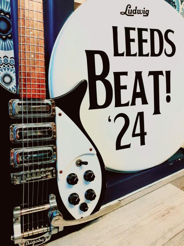 A black guitar to the left of a drumskin that read Leeds Beat '24