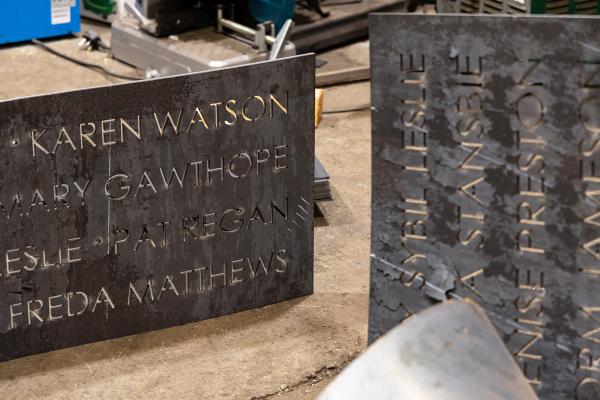 Photograph of two corton steel "ribbons" in production, with the names of some of the nominated women engraved.