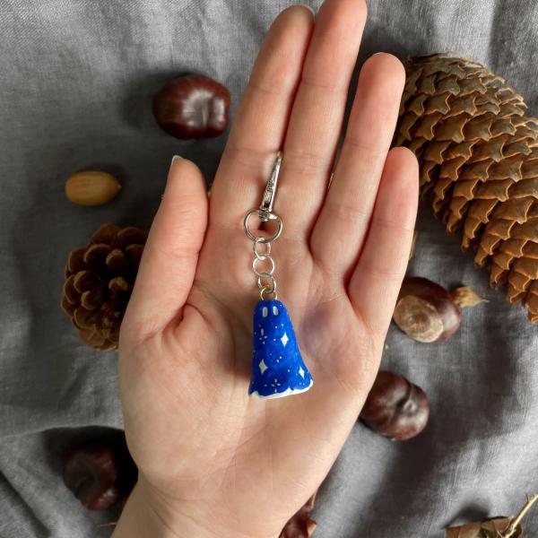 A ghost shaped charm in bright blue with white decoration is being held in the palm of a hand