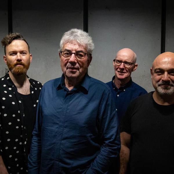 Graham Gouldman and the three other members of Heart Full of Songs smiling at the camera wearing either navy or black on the top.