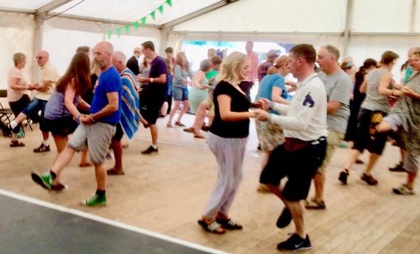 Around 30 people of all ages and genders taking part in a Charleston workshop in a marquis at a festival