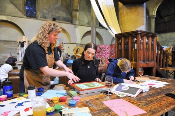 An image of a lady with blonde hair teaching a young person how to screenprint.