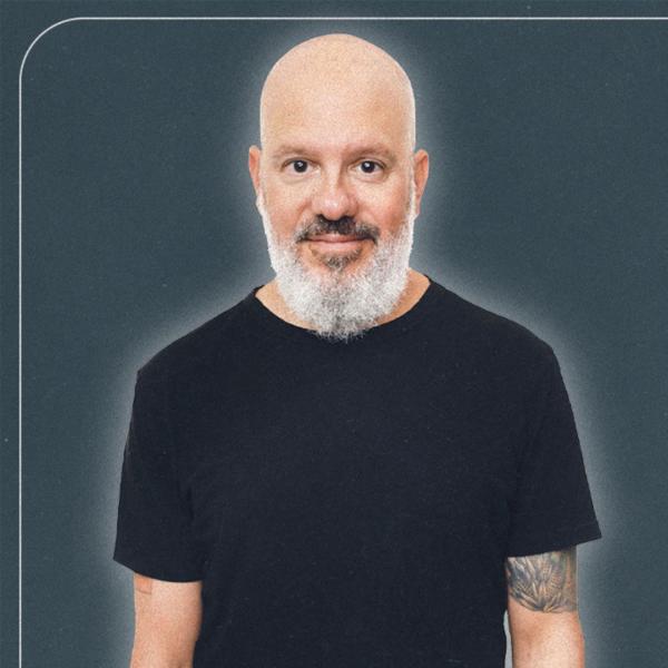 David Cross from the shoulders up with a neutral expression wearing a black t-shirt stood against a charcoal background.