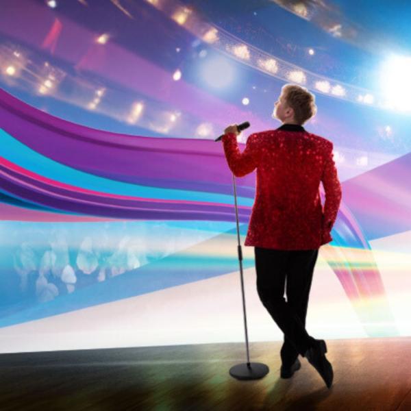 Image of a figure in red sparkly suit jacket and a microphone on a stand taken from behind with lots of colourful lines.