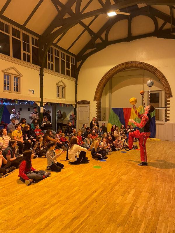 The circus gang gather round to watch the amazing matthew tiffany, dressed all festive, to do a christmas show, with lights and bunting all around