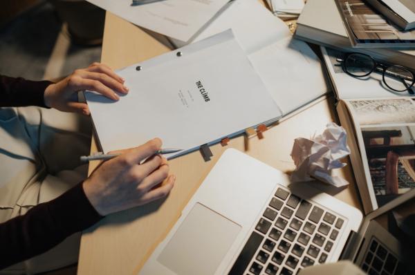 A writer is working on developing their TV script at a messy desk with their laptop open.