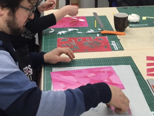 People preparing monoprint plates by adding stencil cut paper shapes