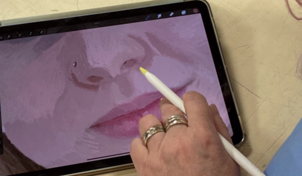 A person's hand holding an iPencil, with an iPad displaying a portrait of person, focussing on their mouth and nose, in shades of pink.