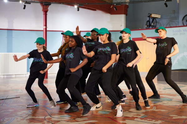 TEMPO street crew in a pose, knees bent and hands out, wearing dark TEMPO t-shirts and turquoise hats. 