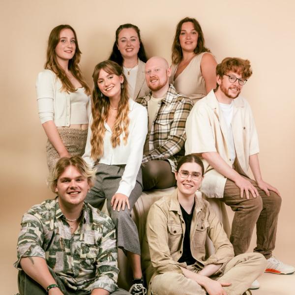 The eight members of The Apex Singers wearing neutral colours and some are wearing camo.